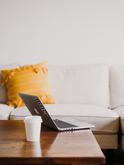 a laptop on a coffee table with a white couch and yellow pillows in the background