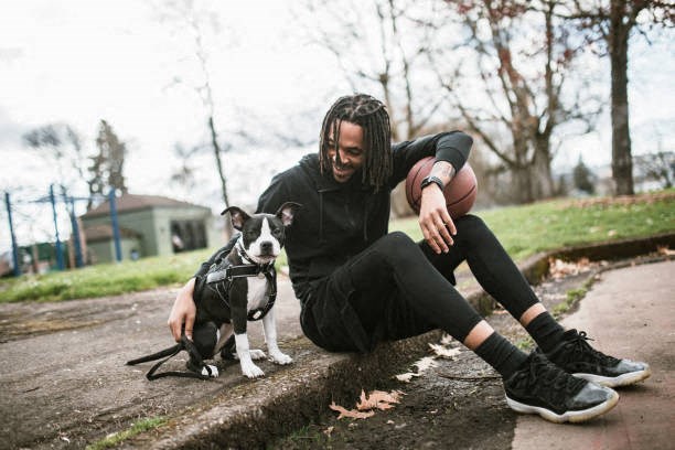 A man with dreadlocks is sitting on the ground with his dog.