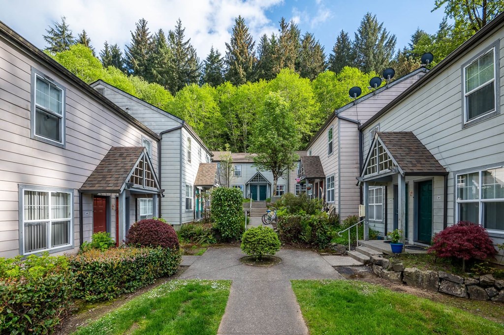 a pathway between two houses with a yard and trees