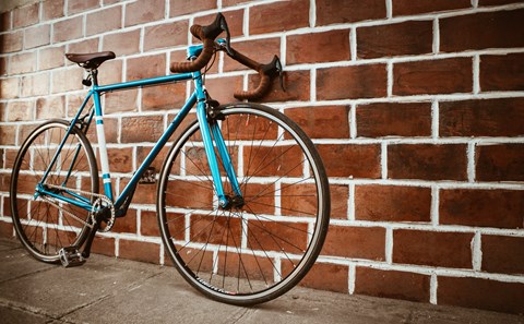 A blue bicycle is leaning against a brick wall.