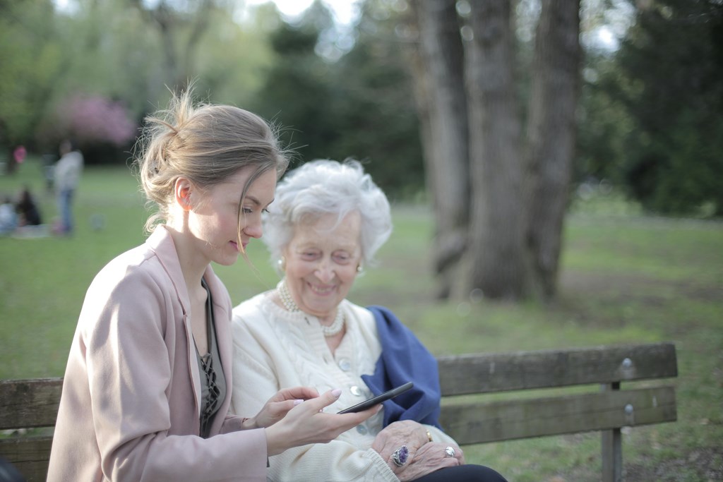 A young woman and an older woman are sitting on a bench in a park.