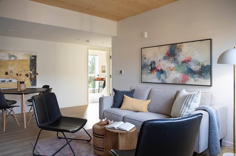 A living room with a grey couch and a painting on the wall.