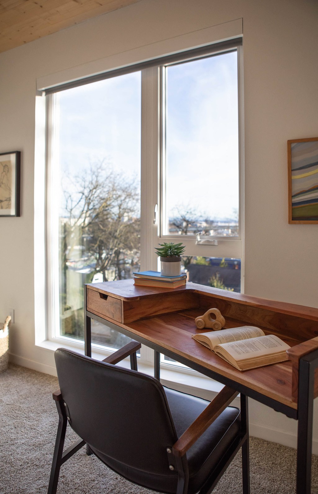 A desk with a chair in front of a window with a view of trees and buildings outside.