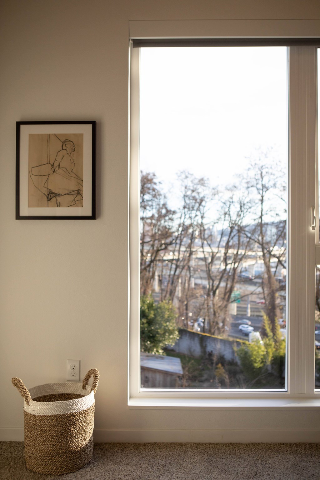 A framed drawing hangs on a wall above a wicker basket.