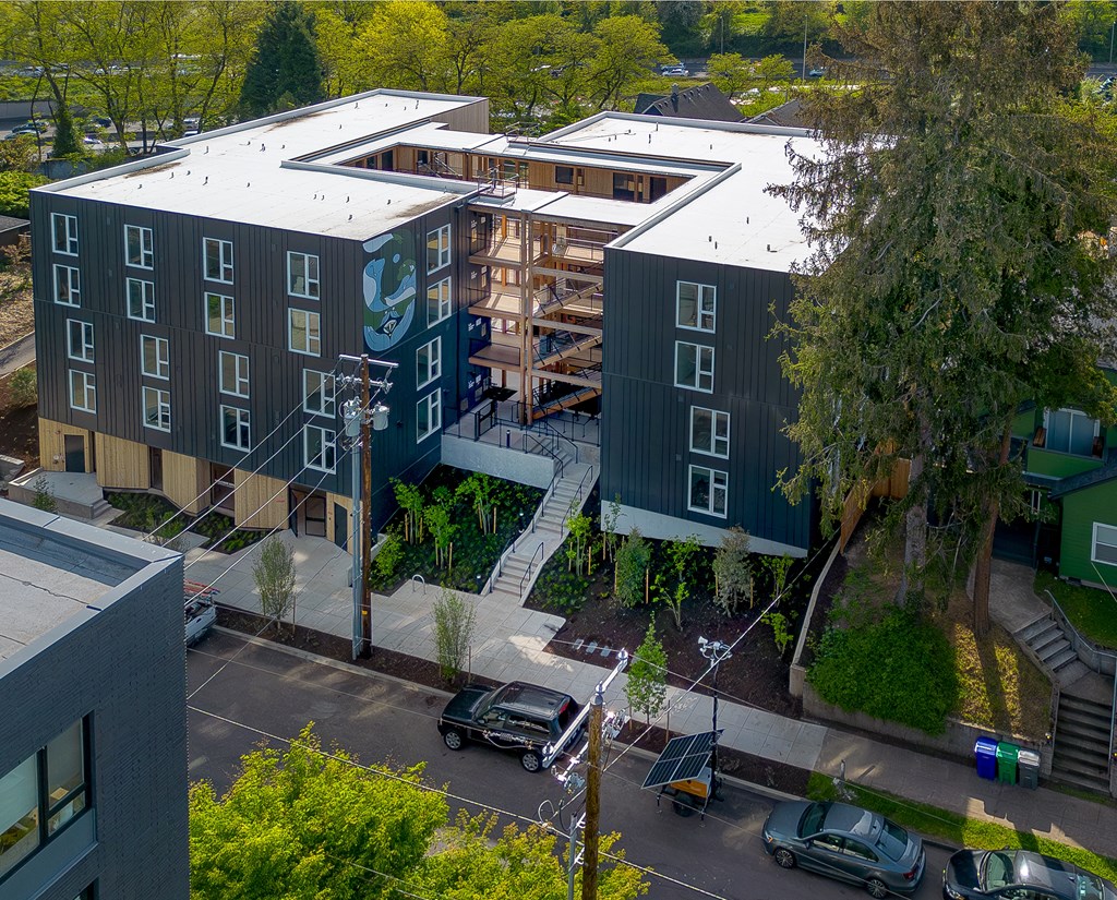 A modern building with a green logo on the side is surrounded by trees and has a parking lot in front.