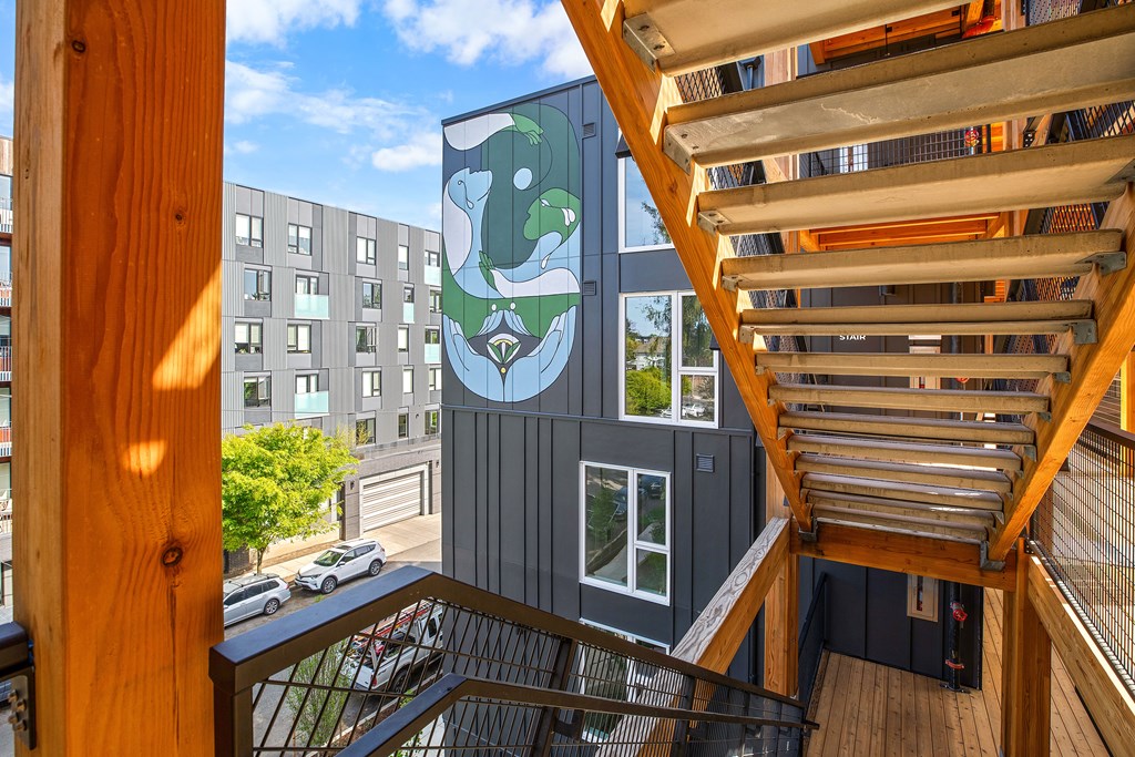 A wooden staircase leads to a balcony with a mural of a bear on the side of a building.