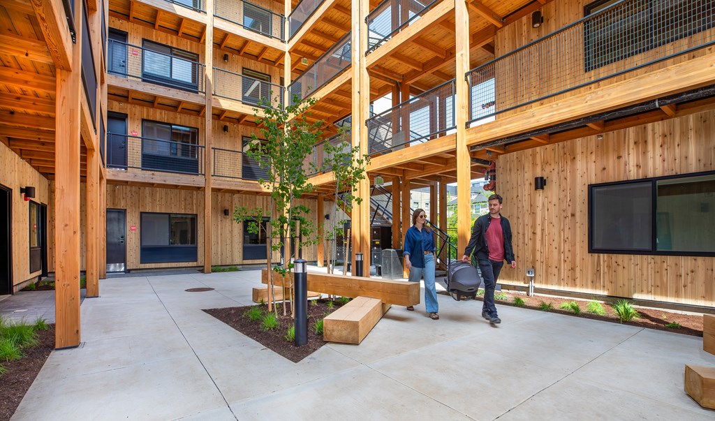 A man and woman are walking through a courtyard with wooden buildings on either side.