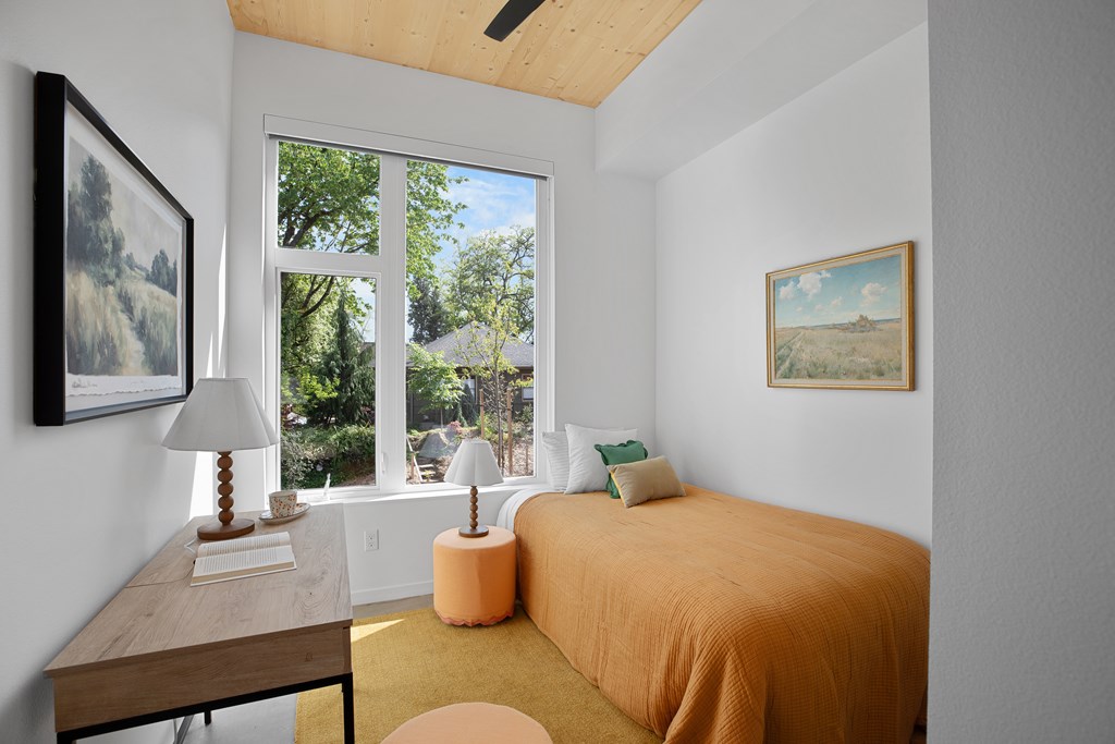 A bedroom with a bed, desk, and two pictures on the wall.