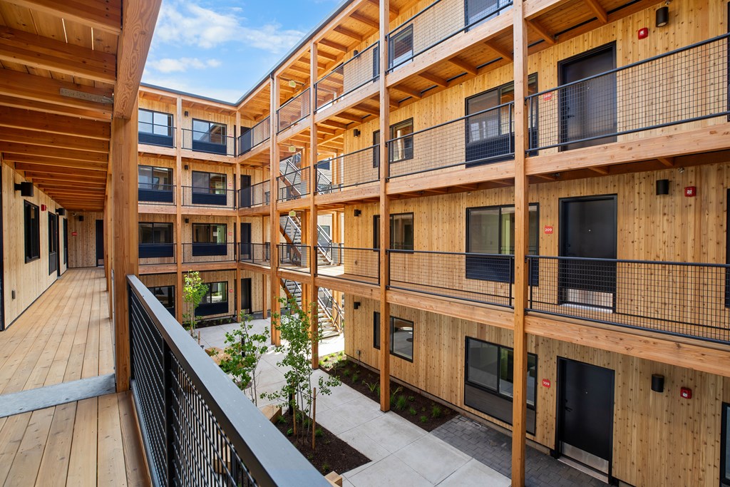 A wooden balcony with black railings and a small garden in the courtyard.
