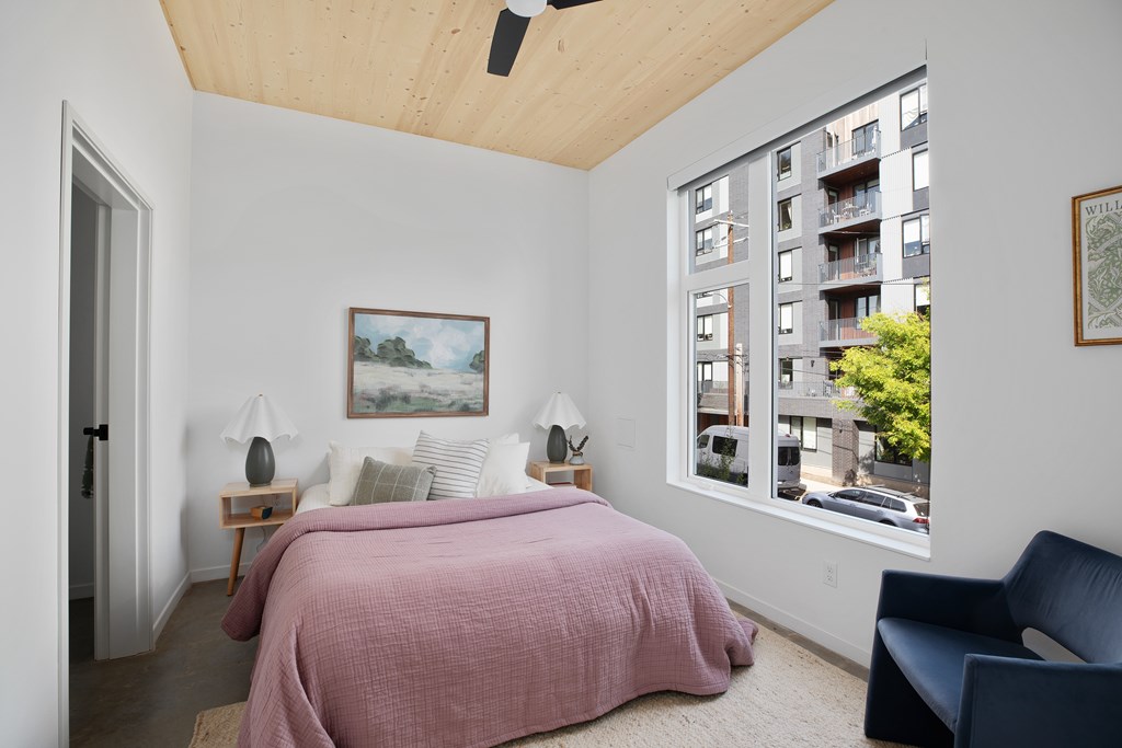 A bedroom with a pink bedspread and a painting on the wall.