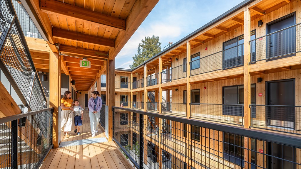 A family is standing on a wooden deck between two buildings.