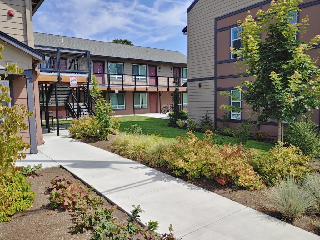 a sidewalk in front of a building with trees and grass