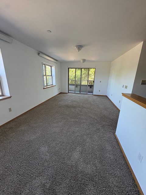 A large empty room with a carpeted floor and a window.