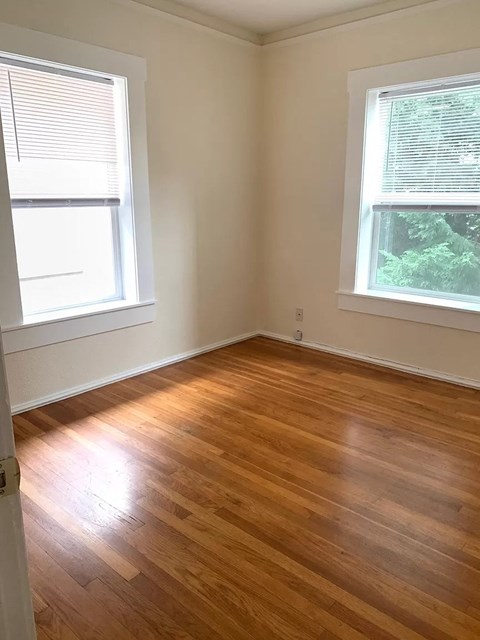 an empty room with a wooden floor and two windows