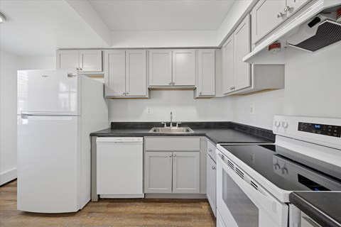 A white refrigerator stands in a kitchen with white cabinets and black countertops.