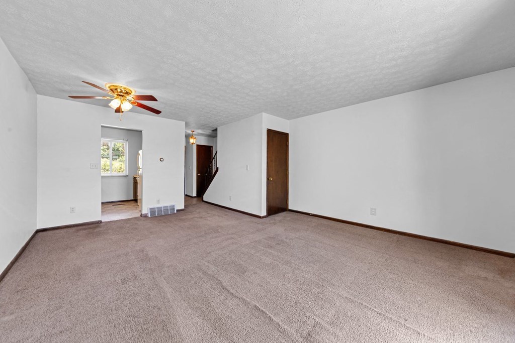 an empty living room with a ceiling fan and white walls