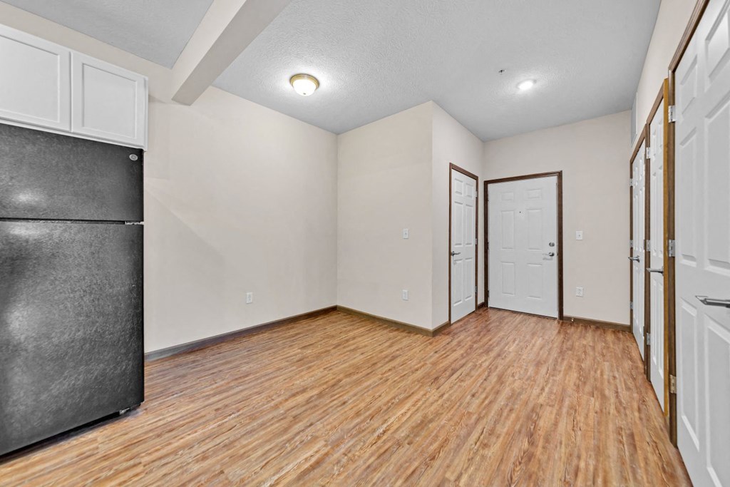an empty living room with wood flooring and a refrigerator