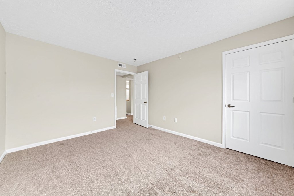 a spacious living room with carpet and a door to a hallway