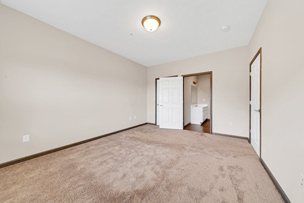 an empty living room with carpet and a door to a bathroom