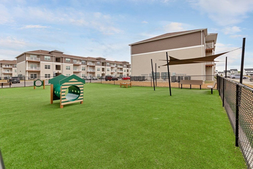 a dog park with a playhouse and a fence with apartments in the background