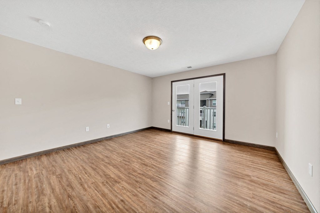 an empty living room with wood flooring and a door to a balcony