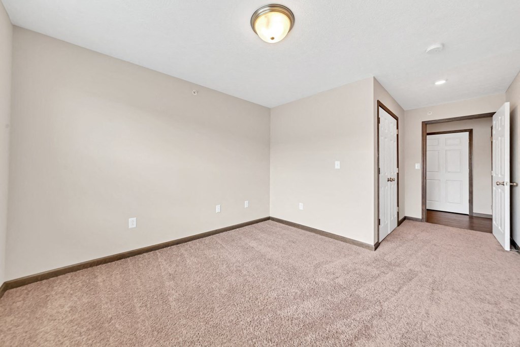 an empty living room with carpet and a door to a bedroom