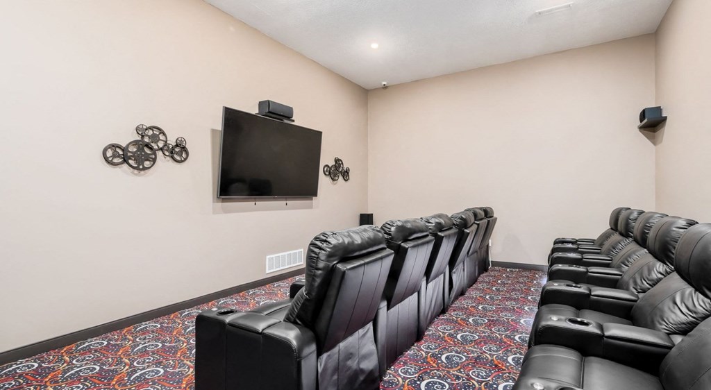 the theater room at our apartments with leather chairs and a tv