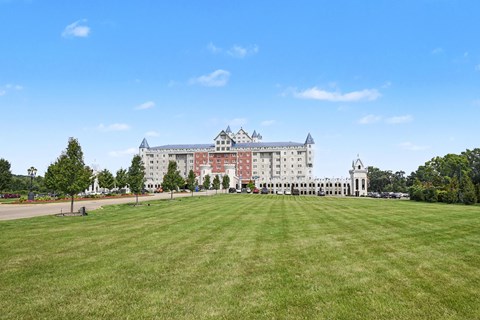 A large white building with a red roof is surrounded by a green lawn.