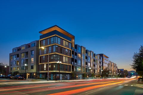 A long exposure shot of a modern apartment building at dusk with light trails from moving vehicles.