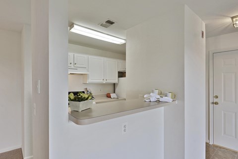 A kitchen with white cabinets and a countertop with a bowl of fruit on it.