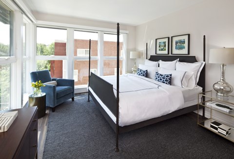 A bedroom with a large bed and a blue chair by the window.