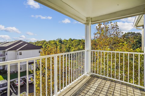 A balcony with a white railing overlooks a parking lot and a building.
