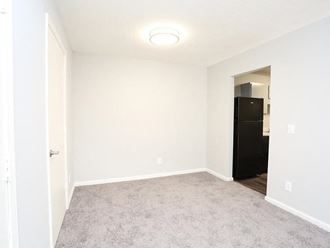an empty room with white walls and a black refrigerator