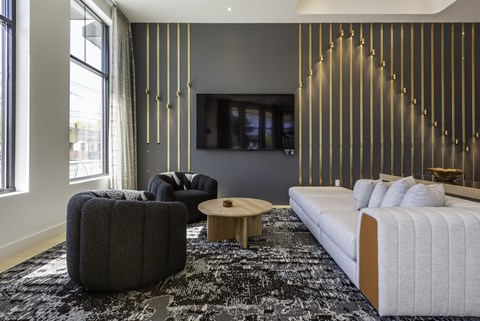 A modern living room with a white sofa, a grey ottoman, and a wooden coffee table.
