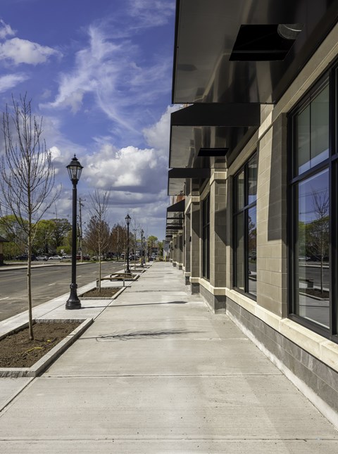 A sidewalk runs down the middle of a street lined with trees and lamp posts.