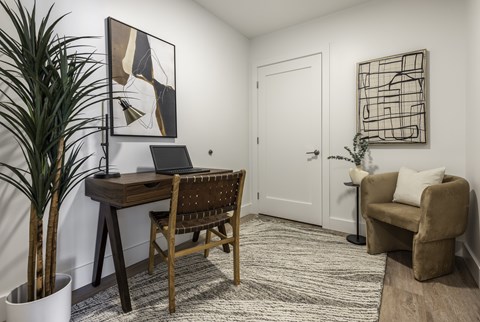 A room with a desk, chair, and potted plant.