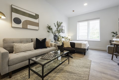 A modern living room with a grey couch, a glass coffee table, and a large abstract painting on the wall.
