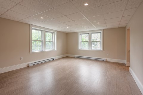 A spacious room with wooden floors and two windows.
