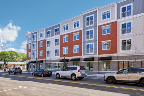 A street view of a multi-story building with cars parked in front.
