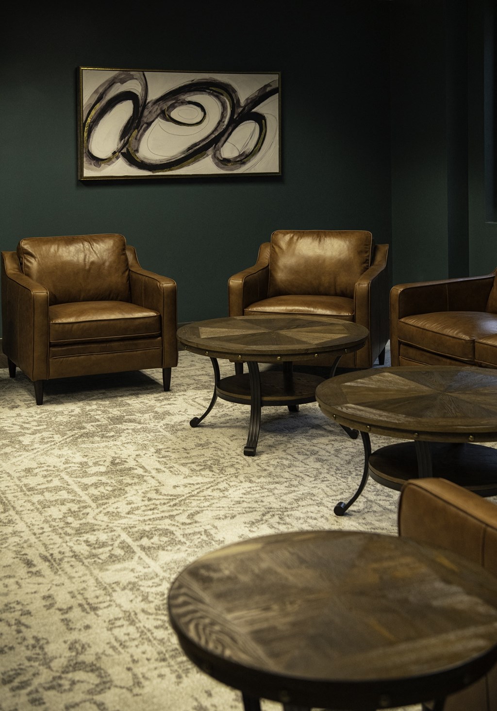 a room with leather chairs and tables and a painting on the wall