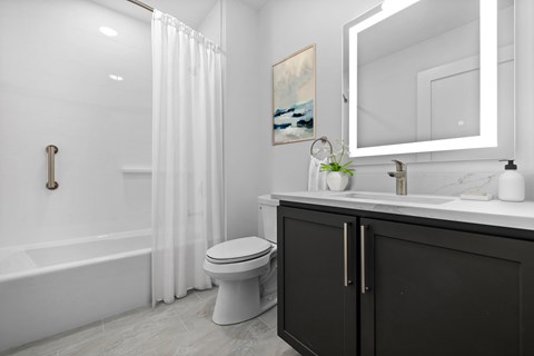 A white toilet sits in a bathroom with a black cabinet and a white bathtub.