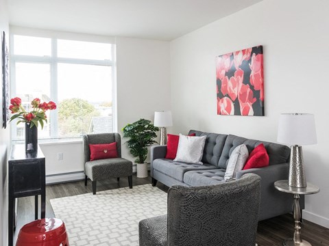 A grey couch with red pillows sits in a living room with a grey chair and a red ottoman.