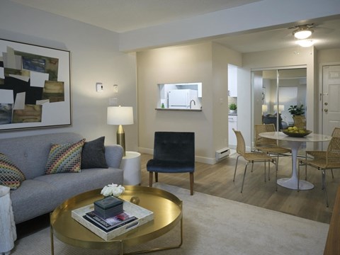 A modern living room with a grey couch, a gold coffee table, and a large painting on the wall.