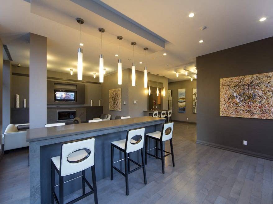 a bar with white chairs and a gray countertop in front of a living room with a