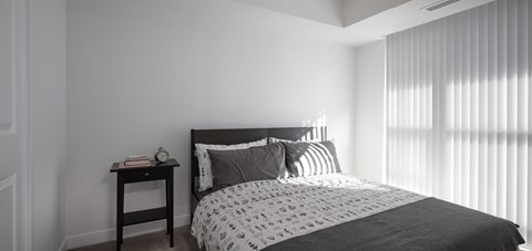 A bedroom with a bed, nightstand, and window with blinds.