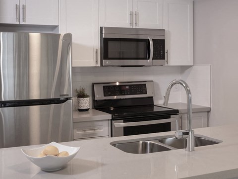 A modern kitchen with a stainless steel refrigerator, microwave, oven, and sink.