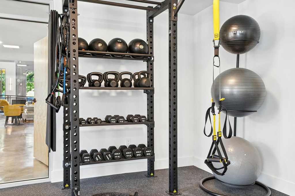 A gym with a rack of kettlebells and a suspension trainer.