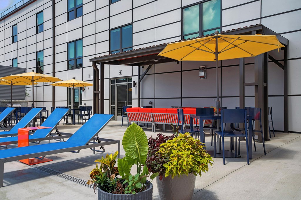 A patio with blue chairs, a yellow umbrella, and a red bench.