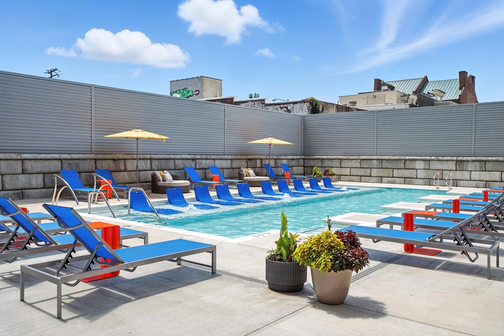 A pool with blue chairs and a bench with a potted plant in front.