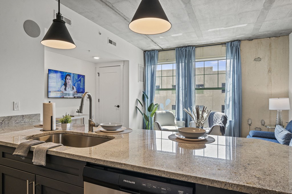 a kitchen counter with a sink and dishwasher next to a living room with a couch and  at The Icon, Richmond, VA, 23230
